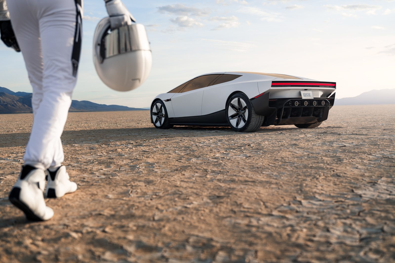 A driver in a white race suit carrying a helmet walks towards the white Tesla Roadster on a desert salt flat